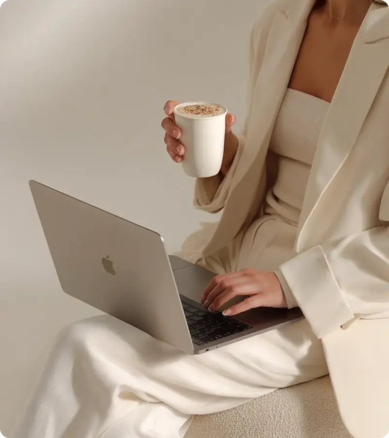 Woman holding coffee, using laptop